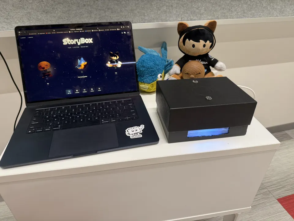 The real StoryBox prototype on a desk beside a laptop and toys